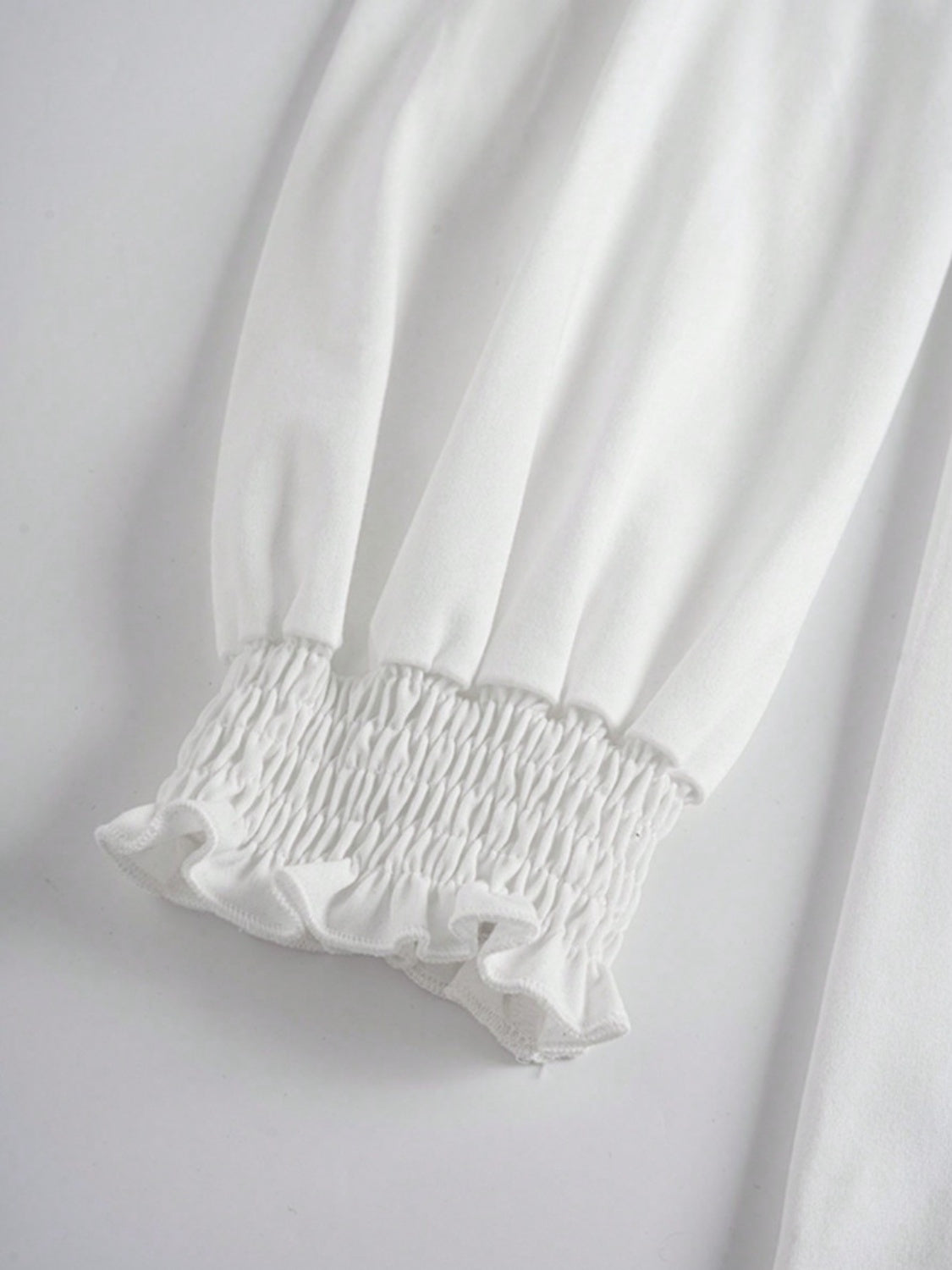 White tunic top with smocked ruffled cuffs and voluminous sleeves.