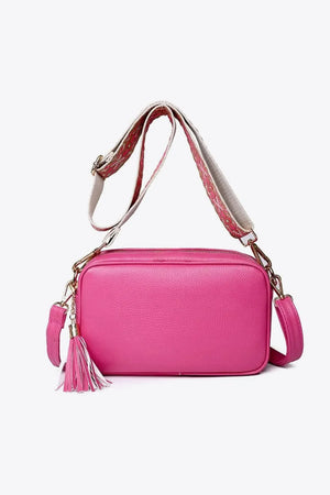 Textured crossbody bag in fuchsia pink with tassel detail and patterned strap.