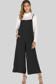 Black culotte overalls with slender straps and wide legs, worn over a white turtleneck.