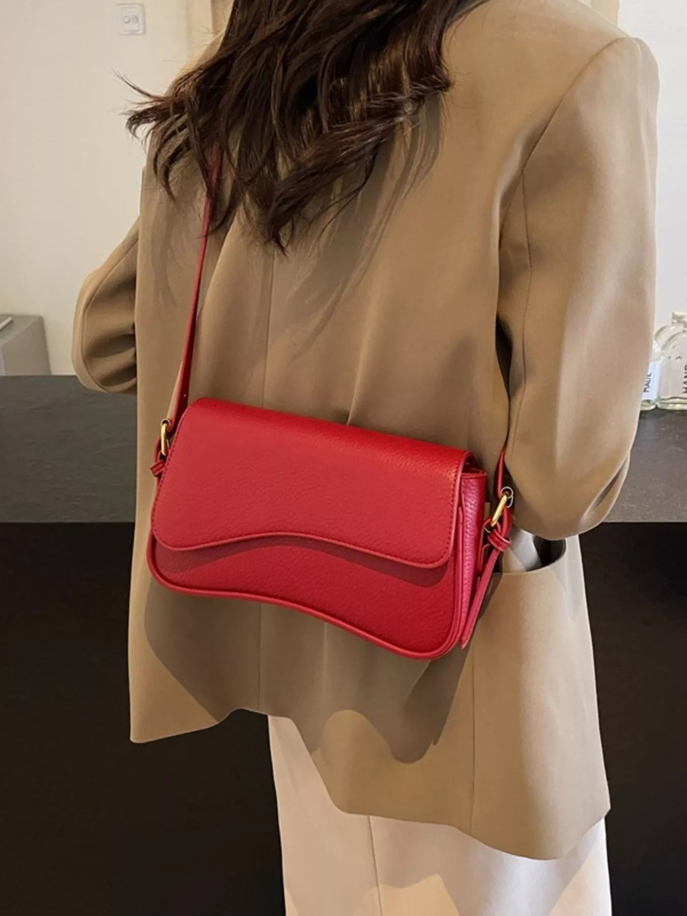 Red faux leather crossbody bag with a curved flap closure.