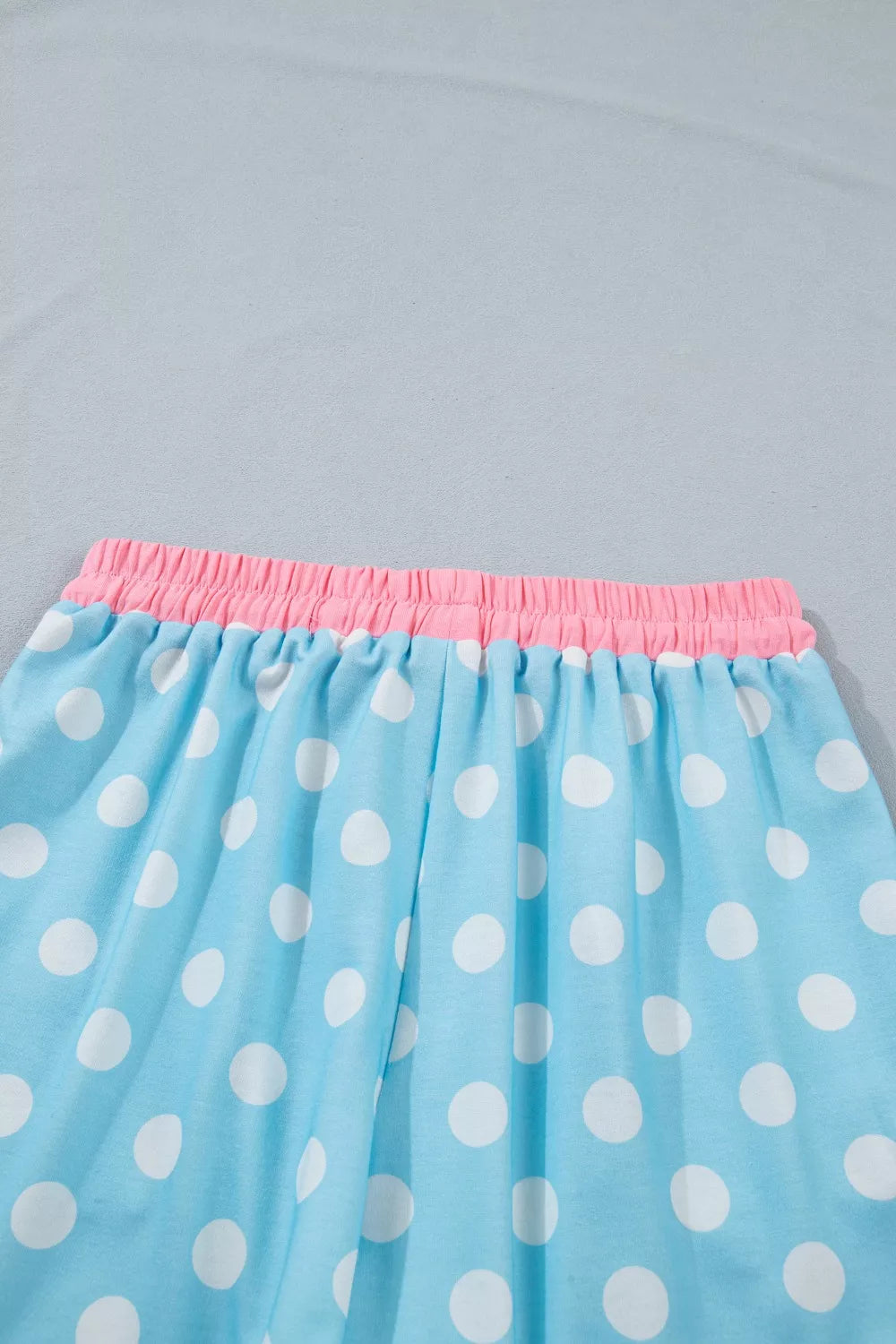 Pastel blue polka dot pajama pants with pink elastic waistband and drawstring detail.