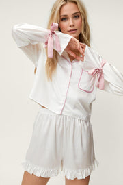 White silk pajama set with pink trim and bow details on sleeves and shorts.