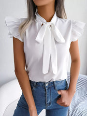 White pussy-bow blouse with ruffle cap sleeves and a tie neck, styled with blue jeans.