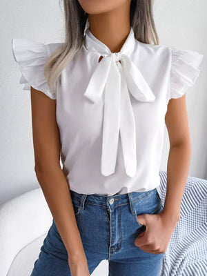 White pussy-bow blouse with ruffle cap sleeves and a tie neck, styled with blue jeans.