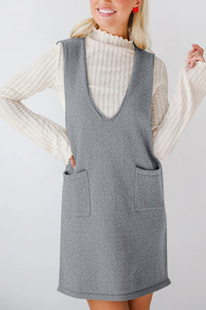Sleeveless gray knit pocket dress with V-neck, layered over a cream ribbed mock neck top.