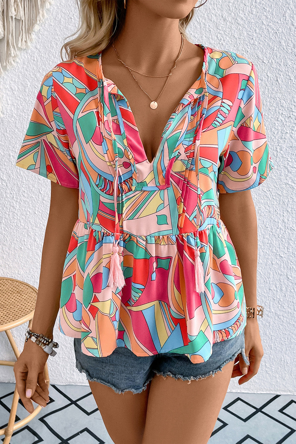 Multicolor geometric print peplum blouse with tassel ties and short sleeves.