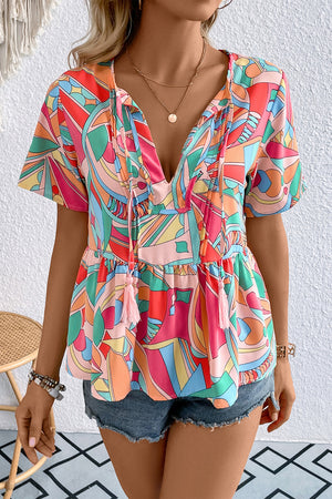 Multicolor geometric print peplum blouse with tassel ties and short sleeves.