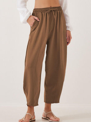 Brown balloon trousers with elastic waist, drawstring, and seamline detail.