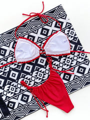 Red ruffle tie bikini set with string bottoms on a patterned towel.