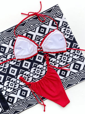 Red ruffle tie bikini set with string bottoms on a patterned towel.