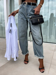 Baggy light wash denim barrel leg jeans with cuffed hems, worn with black heels and a quilted handbag.