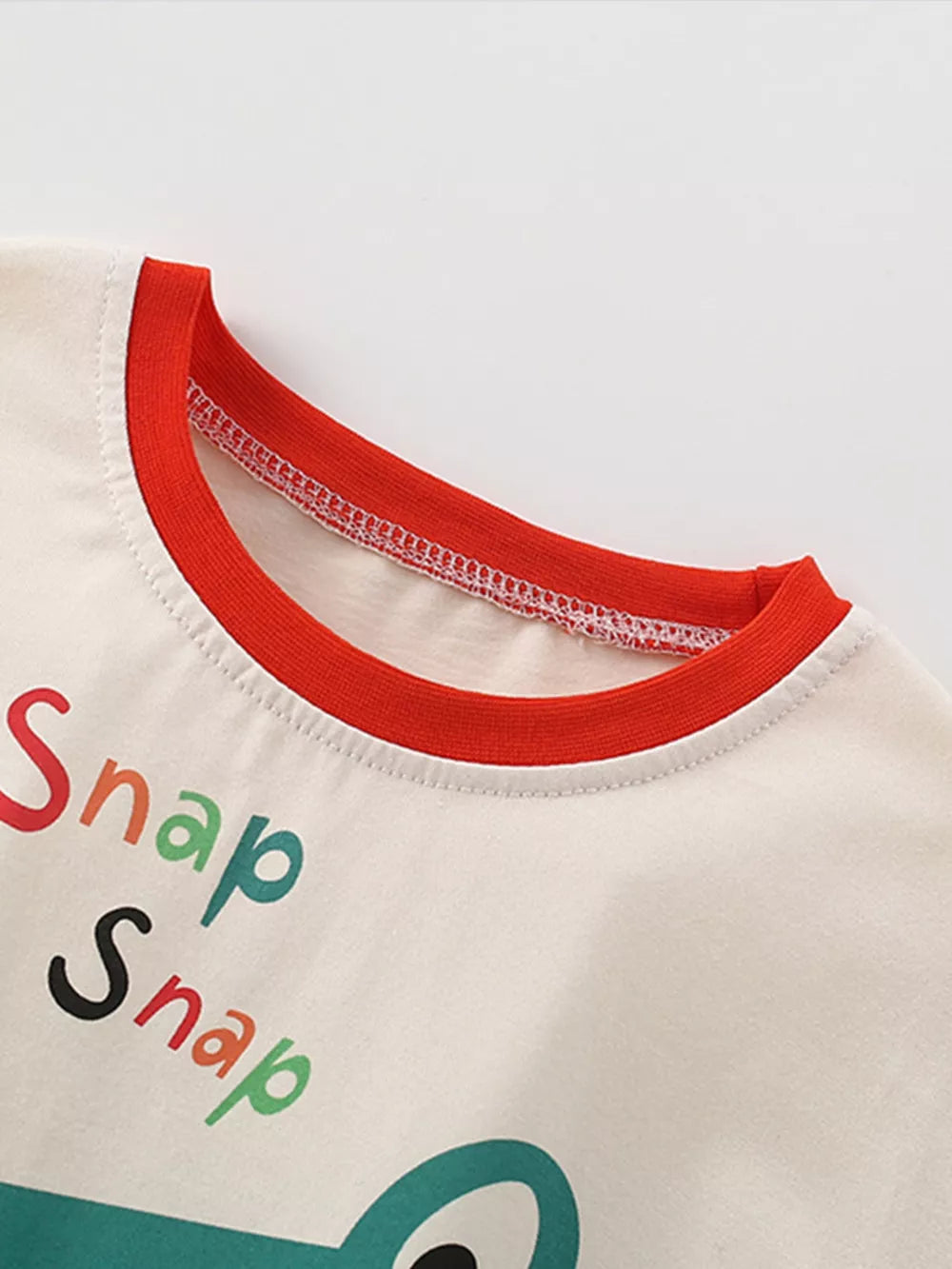 Toddler beige t-shirt with red trim, colorful "Snap Snap" text and dinosaur applique.