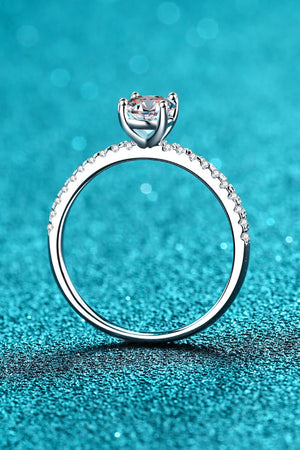Silver moissanite ring with pave band and solitaire diamond on a sparkly blue background.