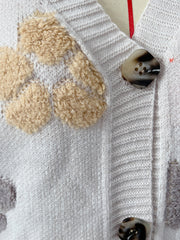 White knit cardigan with floral appliqué detail and tortoise shell buttons.