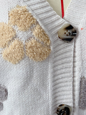 White knit cardigan with floral appliqué detail and tortoise shell buttons.