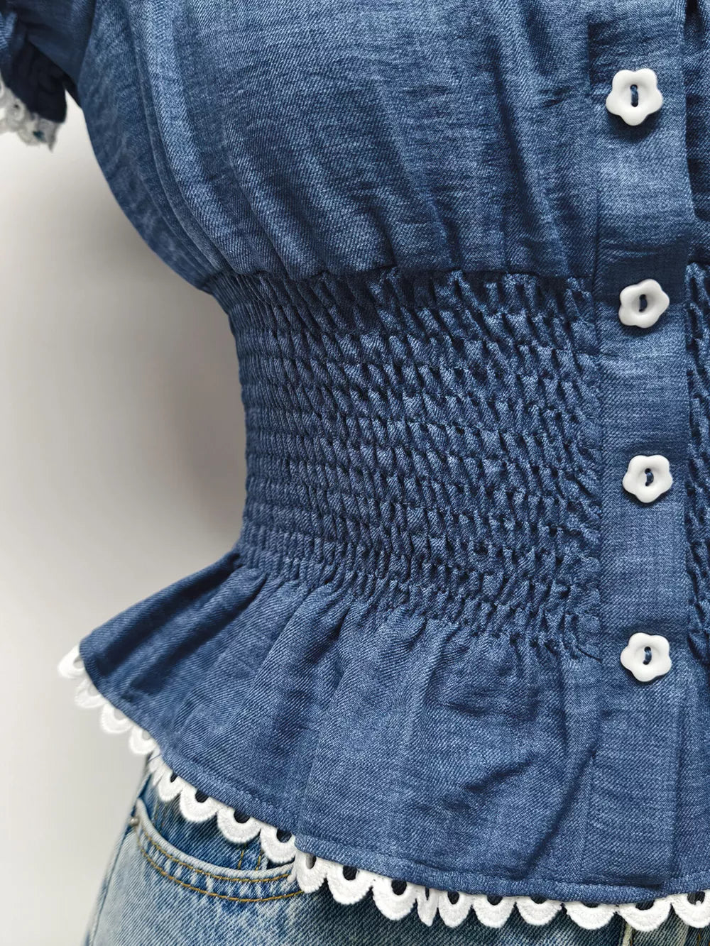 Blue denim maternity blouse with smocked waist, puff sleeves, decorative buttons, and ruffled hem.