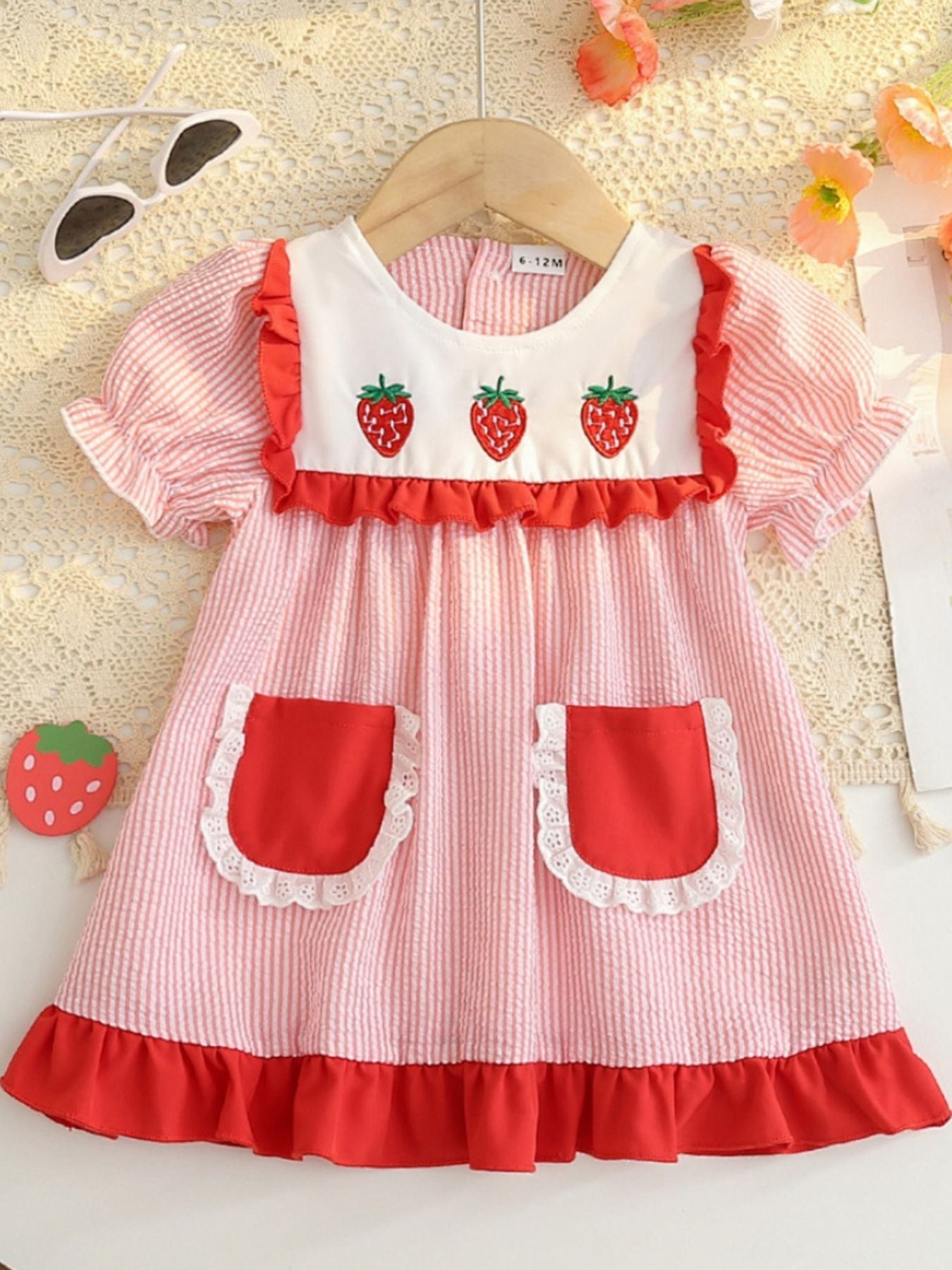 Baby dress in blush pink seersucker with embroidered strawberries and red ruffle trim.
