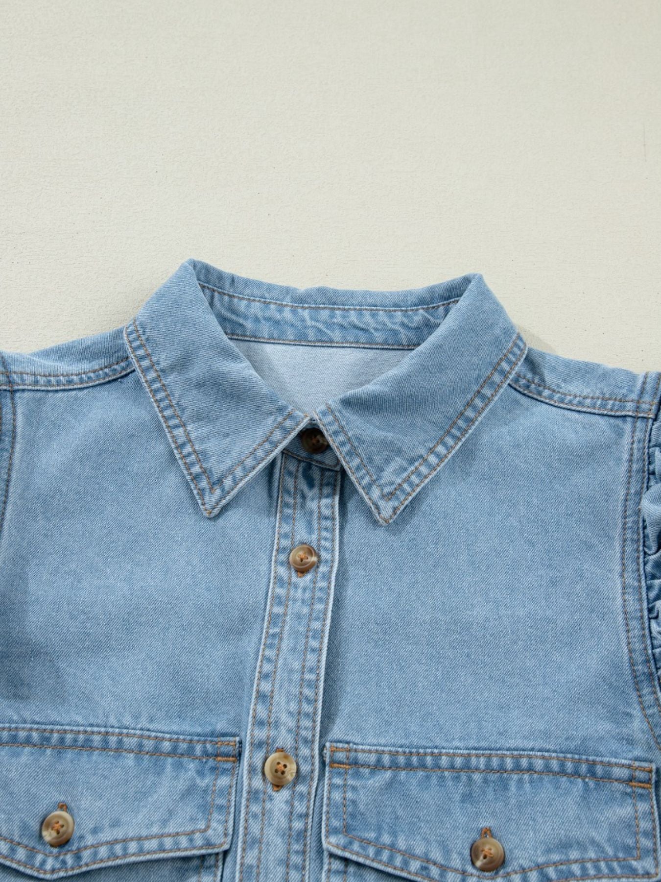 Light blue denim button-down shirt with ruffled sleeves and chest pockets.