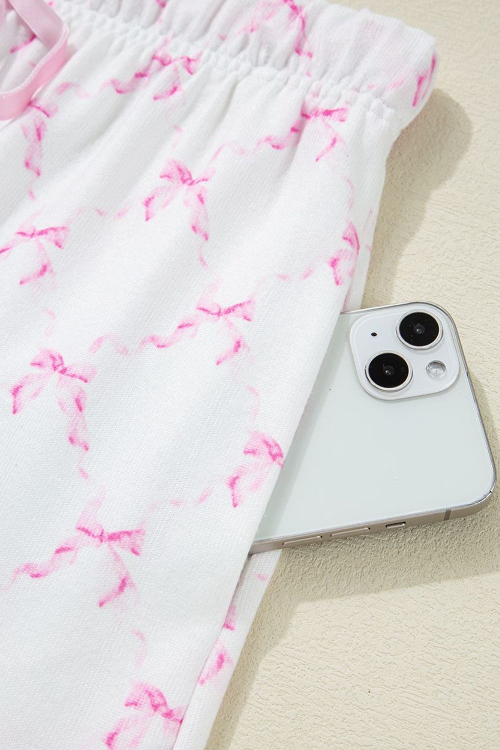 Pink bow print lounge pants with elastic waist and side pocket holding a phone.