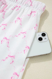 Pink bow print lounge pants with elastic waist and side pocket holding a phone.