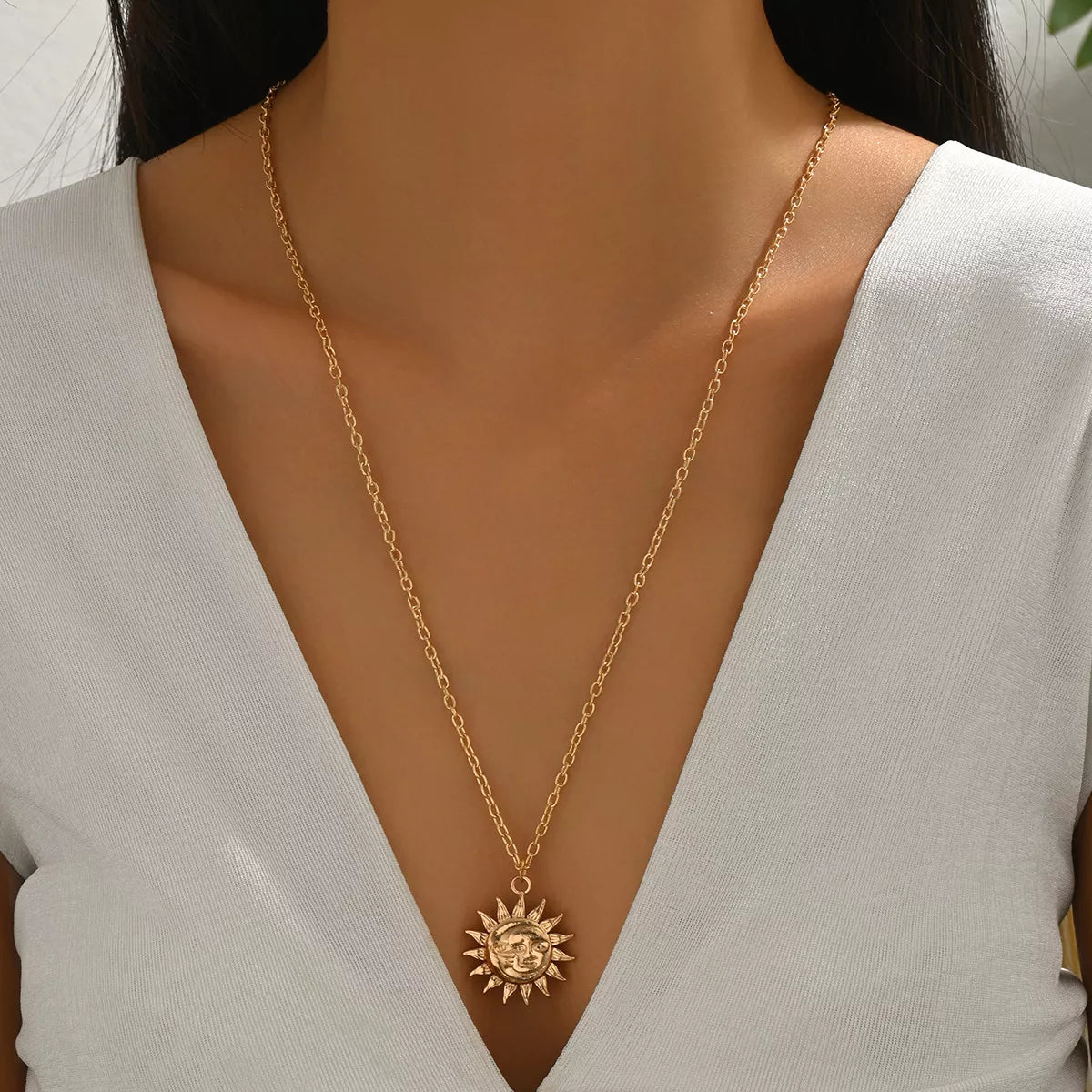 Gold sunburst pendant necklace with a detailed face on a delicate chain.