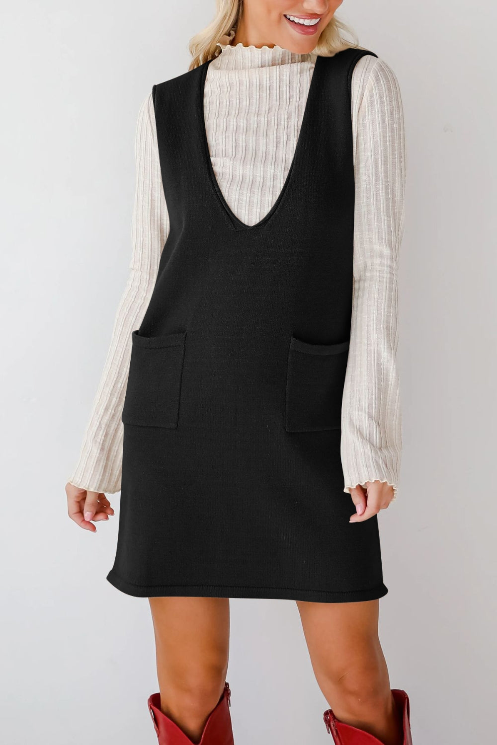Black knit sweater dress with deep V-neck and two front pockets, styled over a ribbed cream top.