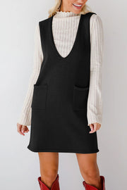 Black knit sweater dress with deep V-neck and two front pockets, styled over a ribbed cream top.