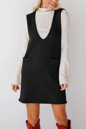 Black knit sweater dress with deep V-neck and two front pockets, styled over a ribbed cream top.