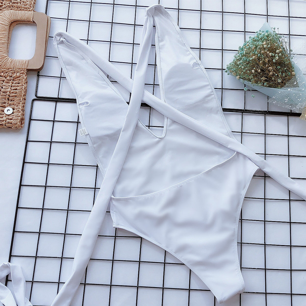 White wrap-around halterneck plunge swimsuit with crisscross straps and a high-cut leg.