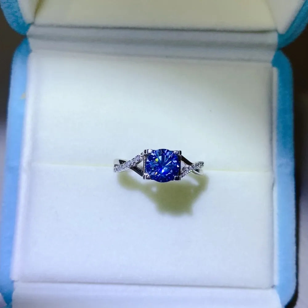 Silver twisted pavé moissanite engagement ring with a blue center stone.
