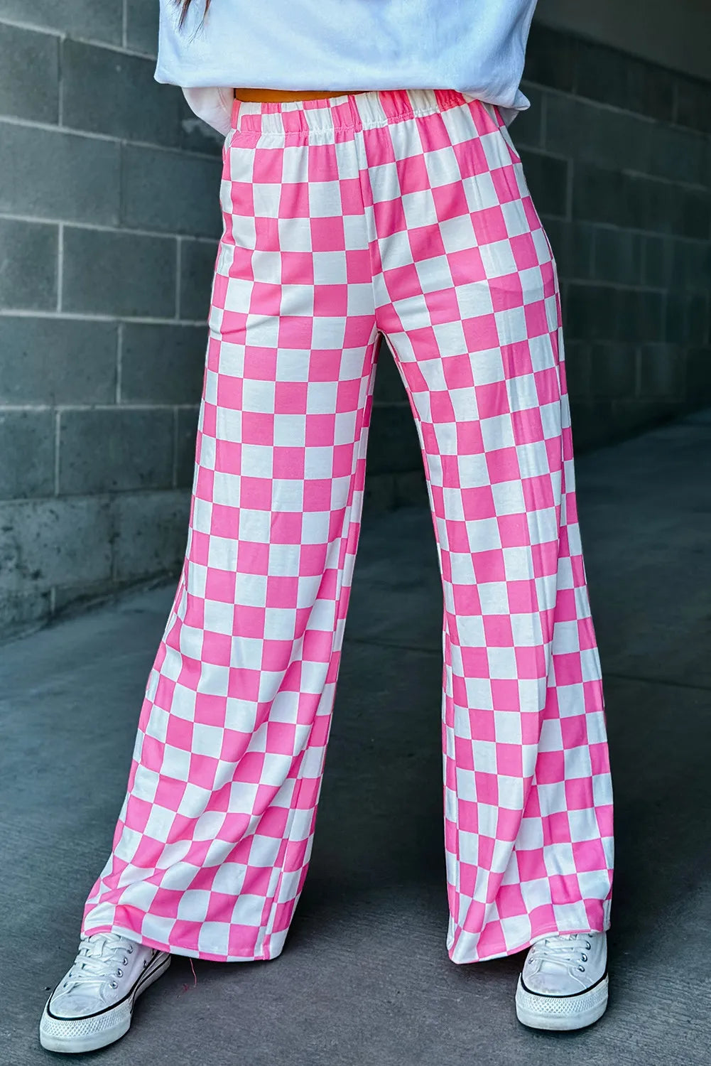 Checkerboard palazzo trousers in fuchsia pink and white with a wide leg, styled with white sneakers.