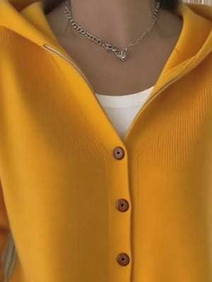 Yellow hooded knit cardigan with button front and wooden buttons, worn over a white top.