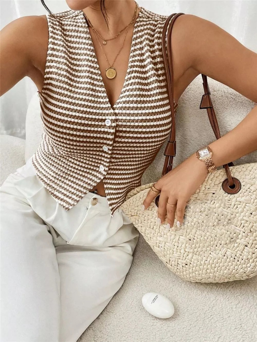 Chic striped knit v-neck tank top with button front, styled with white pants and a straw bag.