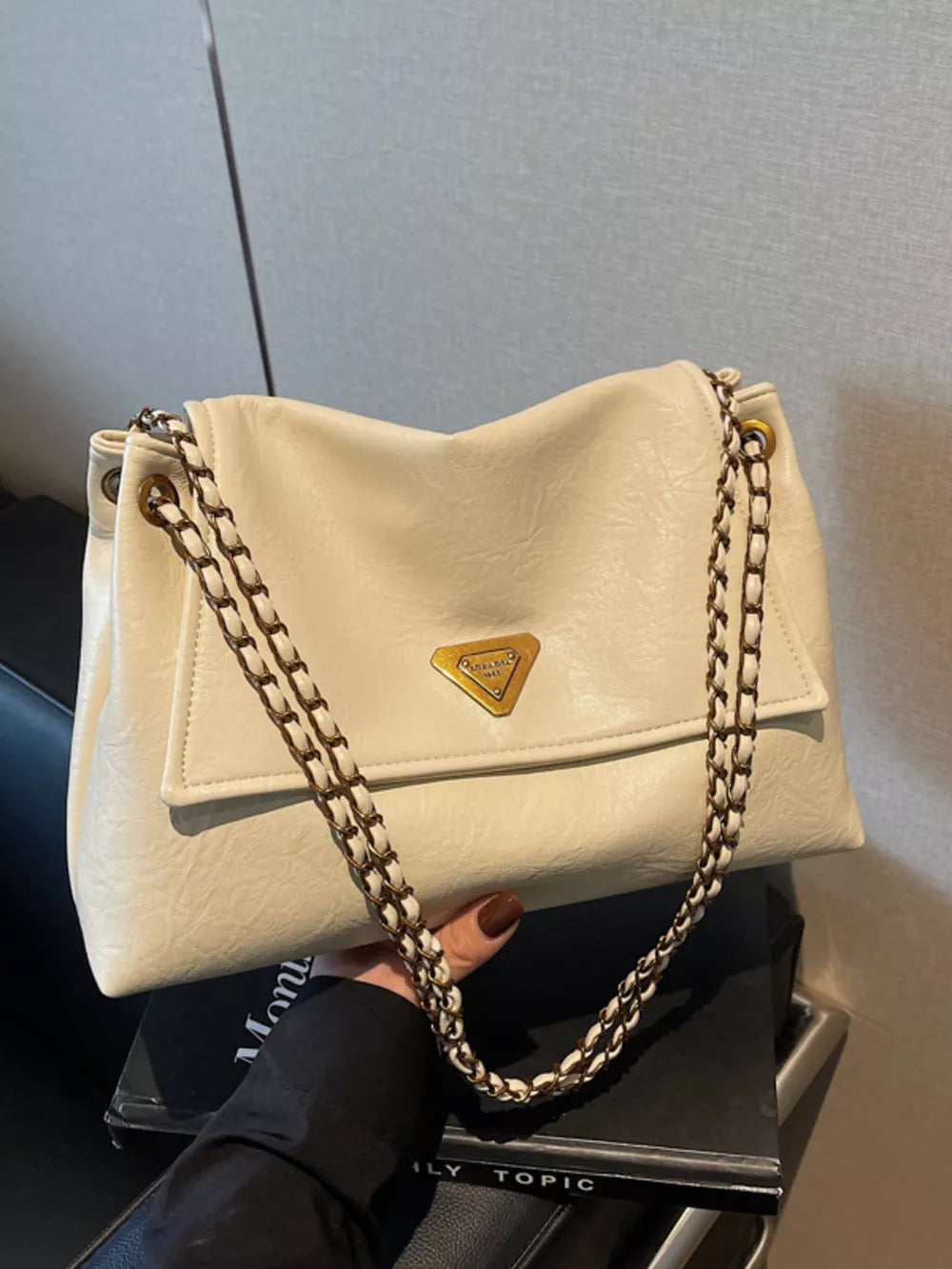 Off-white shoulder bag with chain detail and gold triangle logo.