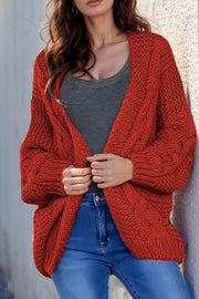 Red cable knit open-front cocoon cardigan with chunky knit texture and relaxed fit.