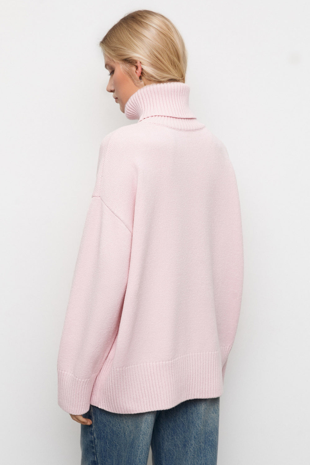 Oversized pink turtleneck sweater with ribbed cuffs and hem, styled with jeans.