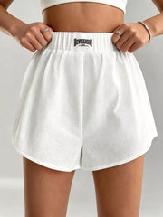 White cotton chino shorts with elastic waistband and logo tag, relaxed fit.