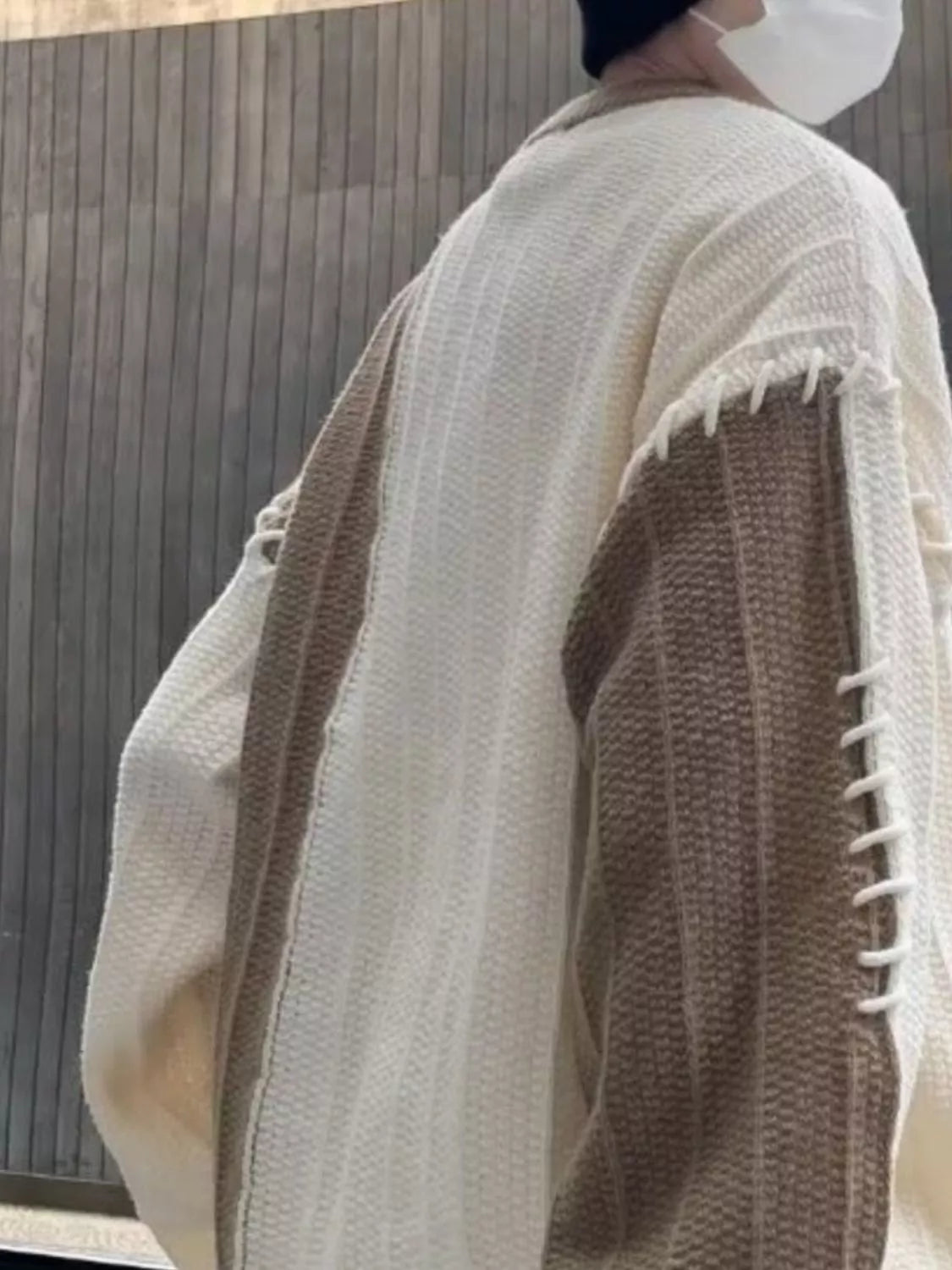 Oversized white sweater with khaki color block sleeves and decorative stitching detail.