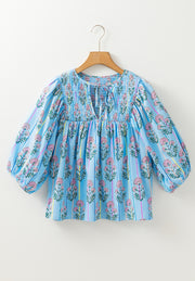 Sky blue floral print smocked yoke blouse with tie neck and puff sleeves.