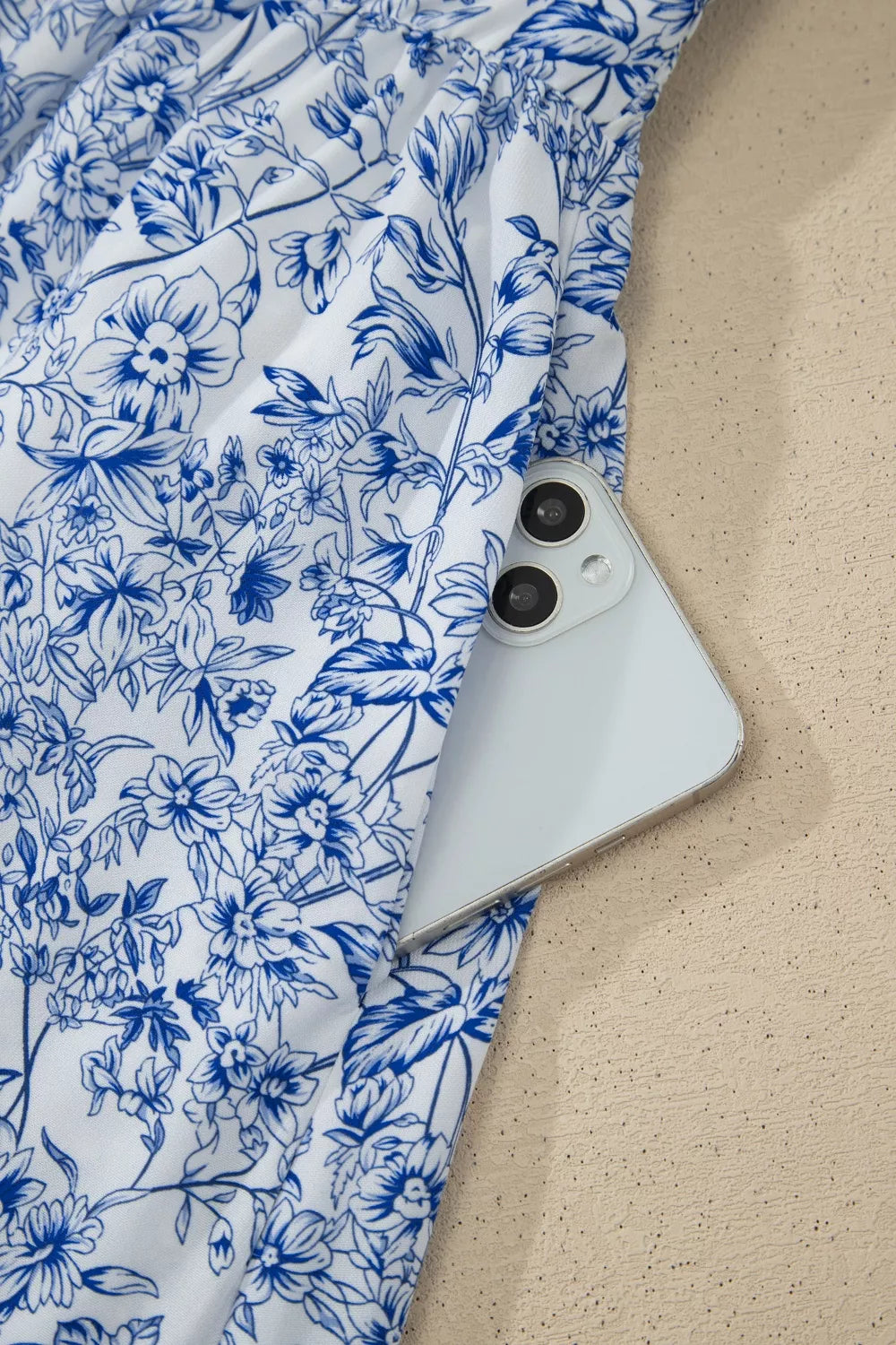 Maxi dress with blue floral print and side pocket holding a phone.