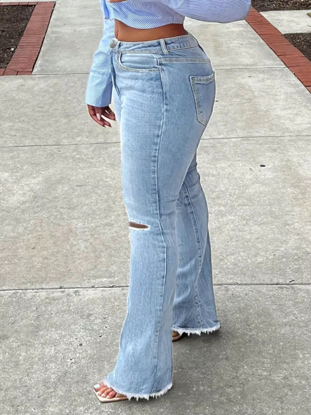 Light blue distressed flare jeans with raw hem and knee rip.