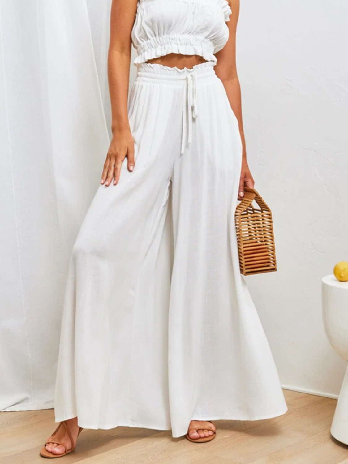 White gathered waist wide-leg palazzo pants with drawstring detail and flowy silhouette.