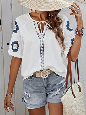 White embroidered yoke sleeve blouse with blue floral details and tie neckline.