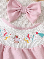 Blush pink baby one-piece with smocked white bodice featuring embroidered cupcake and confetti.