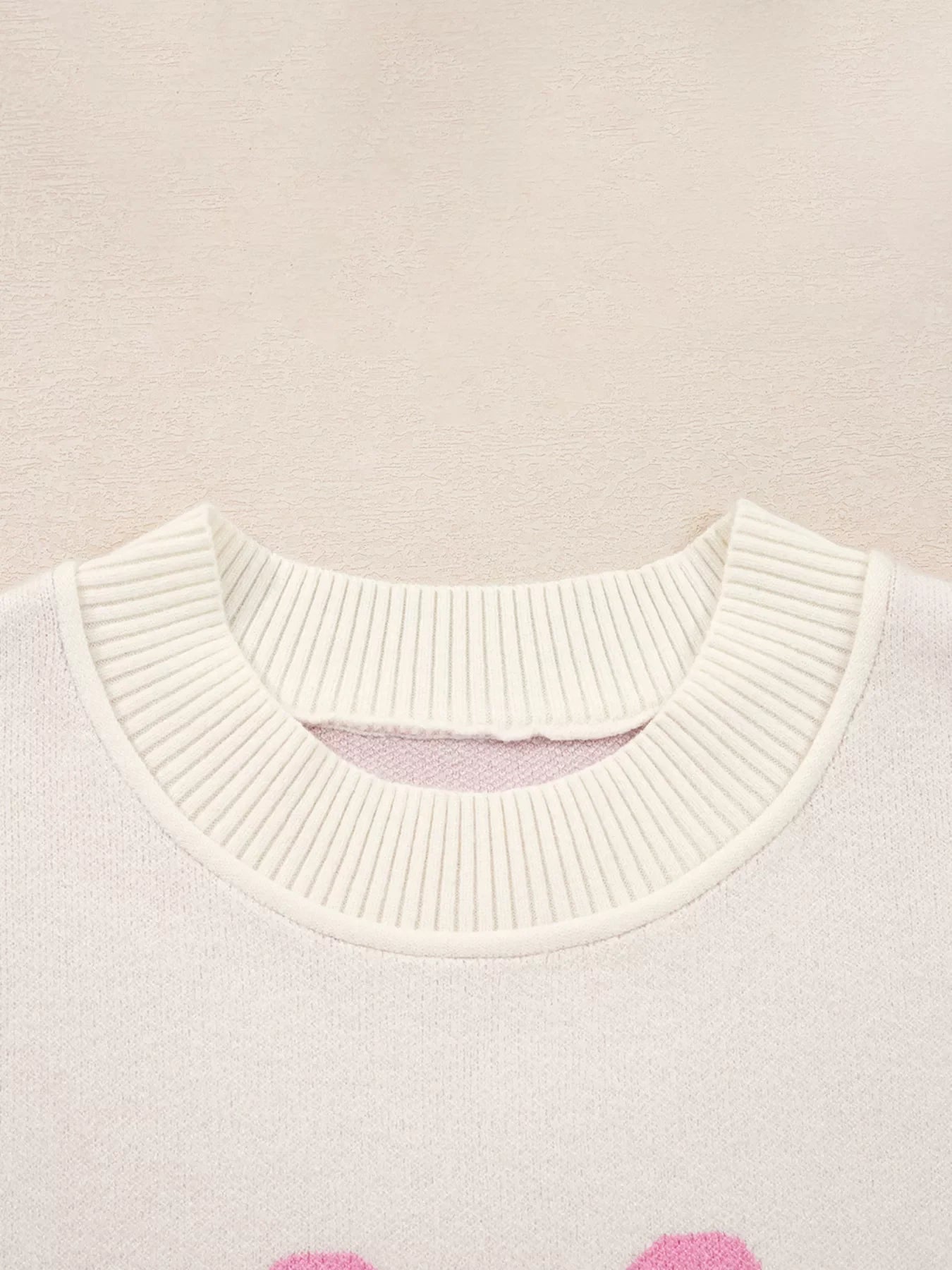 Beige acrylic blend sweater with drop shoulders and a bow print, featuring a ribbed neckline detail.