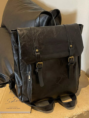 Black pu leather flap backpack with brass hardware and adjustable straps.