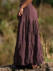 Burgundy tiered maxi skirt with crinkled texture and elastic waist, styled casually.
