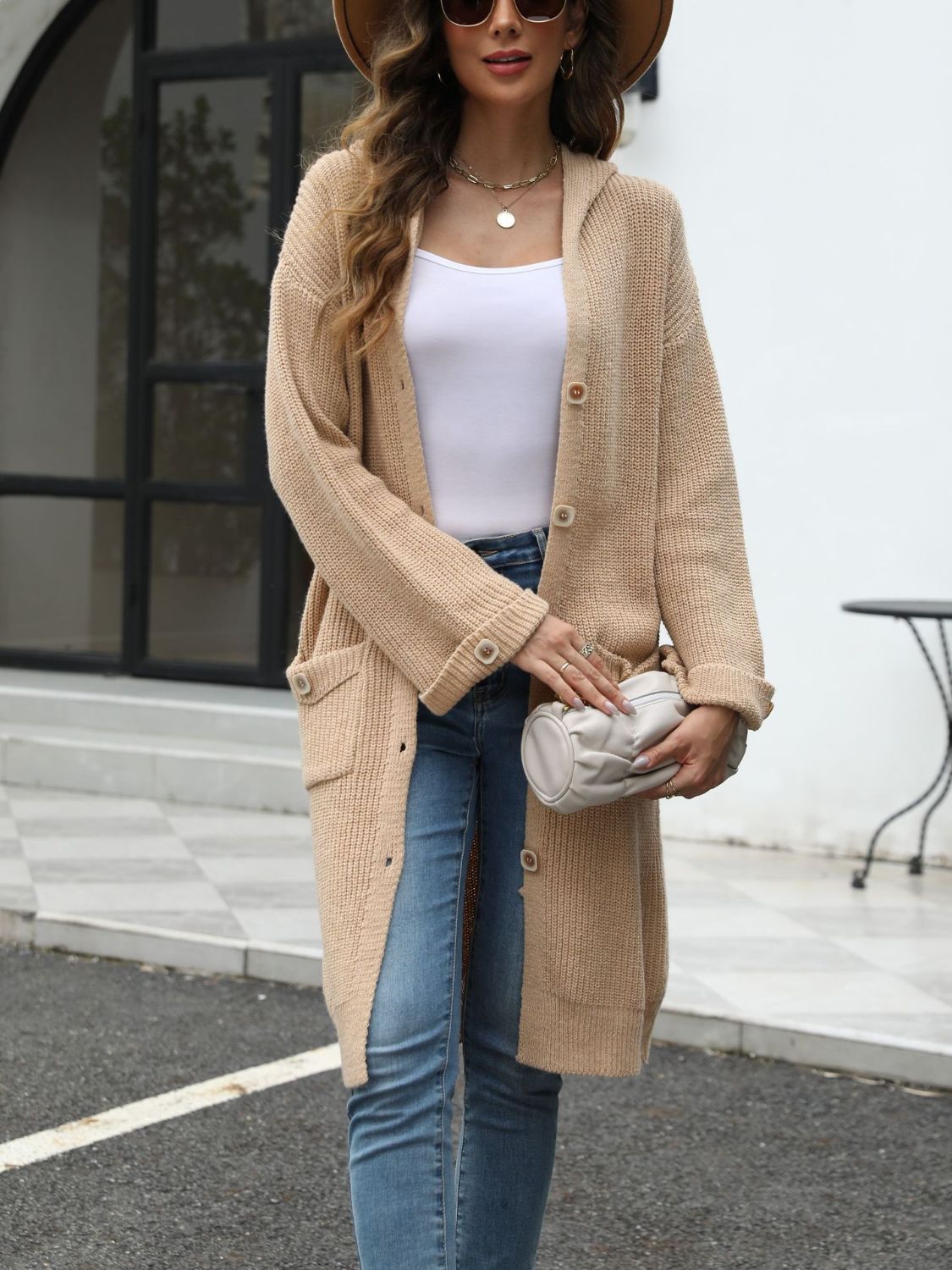 Longline tan knit button-down cardigan with hood and pockets, styled with a white tank and jeans.
