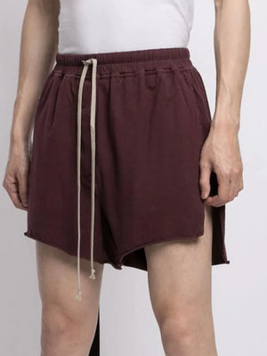 Burgundy lounge shorts with raw hem and side slits, featuring a drawstring waist.