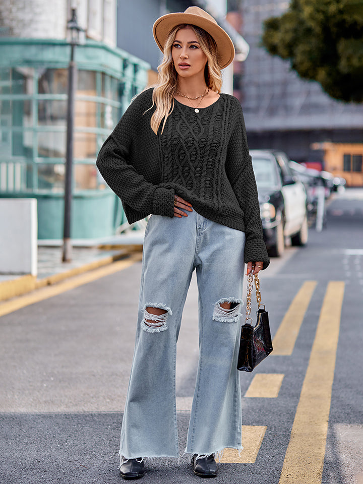 Black cable-knit sweater with a relaxed fit and crew neckline, styled with distressed jeans.